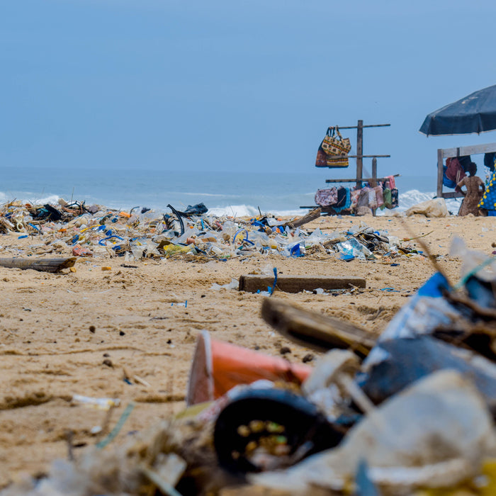 Muovijätettä hiekkarannalla meren rannalla, taustalla aurinkovarjo ja meri.